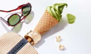 shooting éditorial joaillerie pour le magazine O2 montrant une glace à l'italienne à la pistache posée sur une table à proiximité d'une paire de lunette en écaille rouge et de bagues en or. Elle sort d'un sac à main, et une manchette en or entoure son cône.